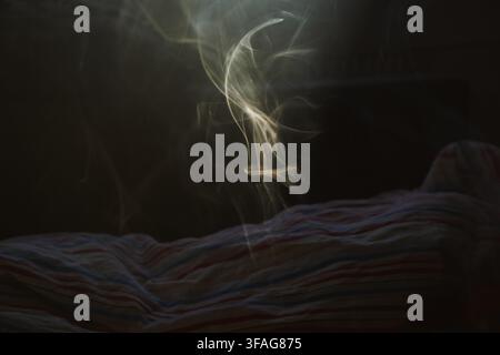 Abstract thin streams of white smoke rising from a striped fabric surface in a dark room creating a mysterious and moody atmosphere with soft lighting Stock Photo
