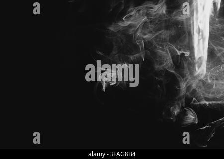 Abstract white smoke swirls and wisps gracefully flowing on a dark black background, creating elegant shapes and fine textured patterns with dramatic Stock Photo