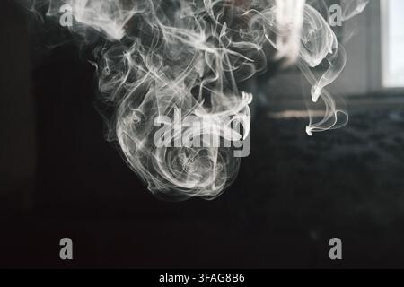 Abstract close-up photography capturing delicate white smoke swirling and curling in dramatic patterns against a moody dark background. Stock Photo