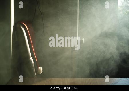 Dense white smoke or mist fills an indoor space, diffusing bright light from a doorway while a red fabric item hangs on a chair in the moody atmospher Stock Photo