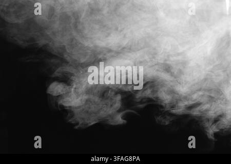 Close-up shot of white smoke swirls and soft vapor clouds flowing gracefully against a dark contrasting background creating an abstract texture. Stock Photo