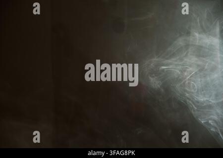 Abstract background featuring delicate wispy white smoke drifting dynamically across a dark moody textured surface with soft lighting and ethereal flo Stock Photo
