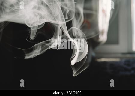 Abstract close-up shot of graceful white smoke swirling and flowing through the air, creating dynamic and intricate fluid shapes against a dark backdr Stock Photo
