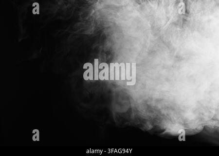 Abstract white smoke swirls and vapor waves billowing against a deep dark black background texture. Stock Photo