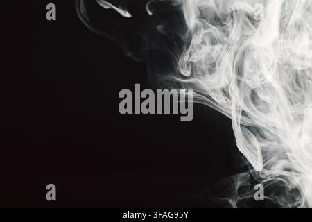 Abstract white smoke swirls and soft vapor wisps flow across a dark background creating a delicate and ethereal texture with dynamic motion and fluid Stock Photo