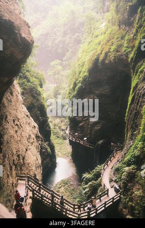 Elevated vertical view of tourists walking along a wooden boardwalk staircase in the steep cliffs of Longshuixia Fissure Gorge in Chongqing, China. Stock Photo