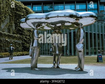 Large stainless steel sculpture of figures holding a cloud-like form outside a modern building in Osaka, Japan Stock Photo