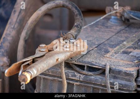 Rusty locking pliers clamping a worn, exposed battery cable in place Stock Photo