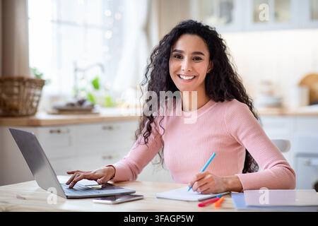 Work From Home. Happy Young Freelancer Lady Working With Laptop In Kitchen Stock Photo