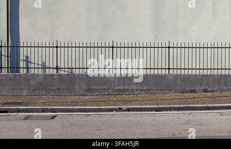 Tubular metal fence on a concrete base at the roadside. Light green plaster wall on behind, sidewalk and street in front. Background for copy space. Stock Photo
