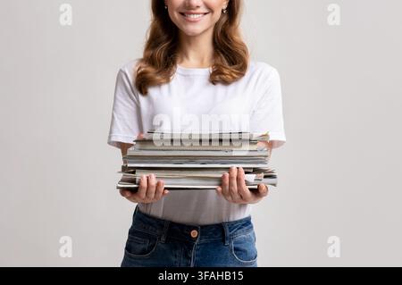 Portrait Of Young Smiling Female Holding Stack Of Old Magazines In Hands Stock Photo