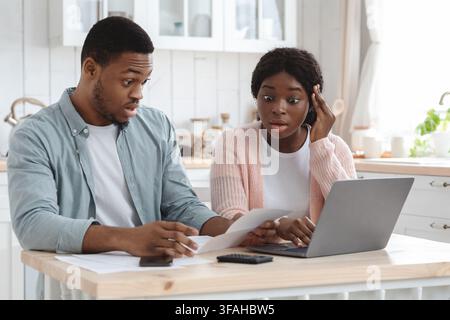 Portraif Of Shocked Black Spouses Checking Financial Documents In Kitchen Stock Photo