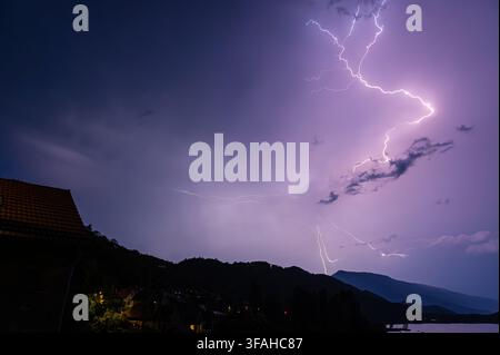Massive flashes of ligthning in a sotrmy sky above a lake and a village at night, southeastern France Stock Photo
