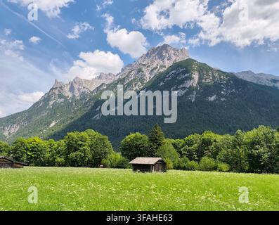 Picturesque summer landscape with a small wooden hut in a lush green meadow beneath the majestic Karwendel mountains in Mittenwald, Bavaria, Germany Stock Photo