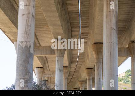 A perspective view looking up at the underside of a large concrete highway structure supported by numerous thick pillars and beams Stock Photo