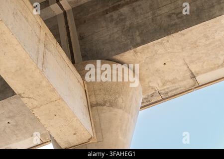 Close-up perspective of the underside of a modern concrete overpass showing structural beams and a large support pillar Stock Photo