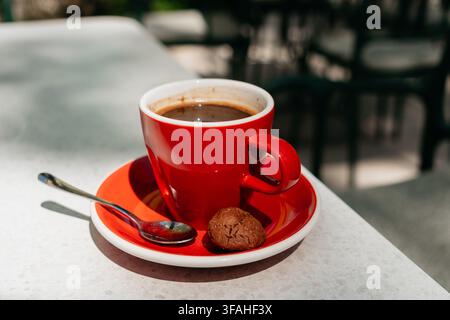 Fresh americano served in a red ceramic cup with cookie on a bright table. Smooth flavor and premium coffee moment create a stylish cafe lifestyle Stock Photo