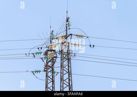 Close-up view of electrical transmission towers supporting numerous wires and insulators under a bright, cloudless sky Stock Photo