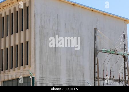 A stark concrete building with a repeating pattern of narrow windows stands beside a weathered utility pole carrying electrical insulators and wires Stock Photo