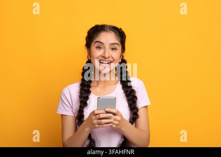 Indian woman using smartphone isolated on yellow background Stock Photo