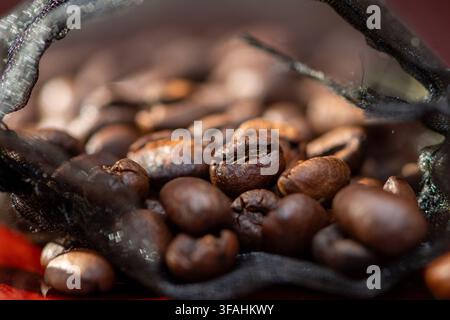 Roasted coffee beans are shown in closeup inside a dark mesh bag. Stock Photo