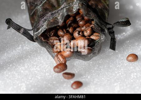 Roasted coffee beans spill from a black mesh bag onto a white surface. Stock Photo