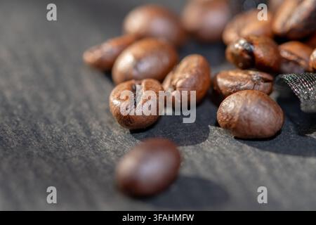 Roasted coffee beans are scattered across a dark textured surface in a close-up macro view. Stock Photo
