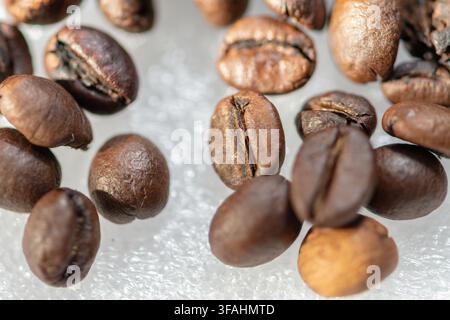 Roasted coffee beans are scattered in a closeup view on a light textured surface. Stock Photo