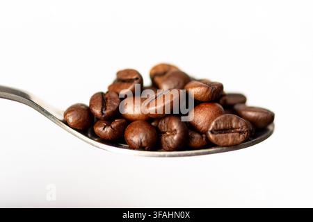 A spoon holds roasted coffee beans against a clean white background. Stock Photo