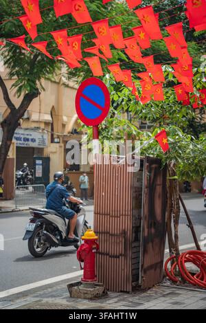 Motorbike passing under red flag canopy near fire hydrant, Hanoi Old Quarter Stock Photo