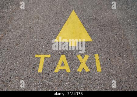 Top down close up view of the word TAXI and a directional arrow painted in bright yellow on coarse gray asphalt pavement in Lugano, Switzerland. Stock Photo