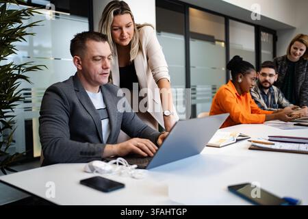Diverse business team collaborating in modern office using laptop Stock Photo