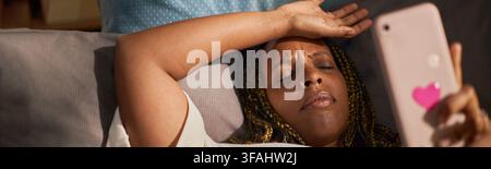 Header of Stressed Black Woman Lying on Sofa and Holding Smartphone Stock Photo