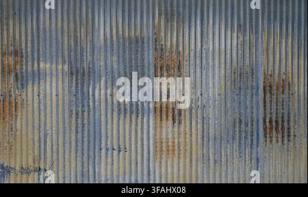 Weathered blue tinted corrugated metal with rust pitting dents holes mineral deposits and worn light yellow paint on galvanized ridged surface Stock Photo