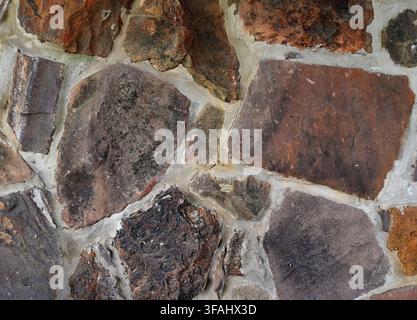 Close up of a multi color rock and mortar wall surface with porous rough uneven stones in varied colors and one lava like stone Stock Photo