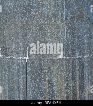 Vertical view of weathered galvanized industrial metal surface with white mineral deposits, rust tint, and seam with rivets and caulk Stock Photo