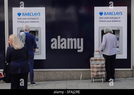 Senior people using outdoor Barclays cash machines to withdraw money or check balances on a street in Liverpool, UK. Stock Photo