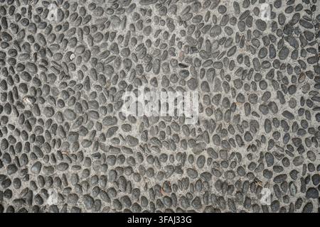 High angle close up view of a round pebble stone pavement set in concrete. The textured surface shows natural grey stones used for outdoor flooring. Stock Photo