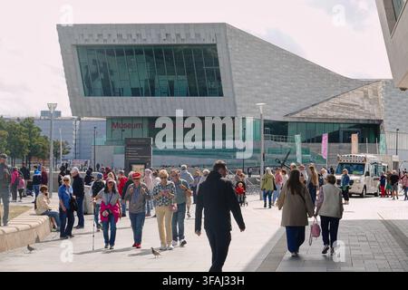 A large crowd of pedestrians and tourists walking in a public plaza outside the modern, striking building of the Museum of Liverpool at Pier Head, UK Stock Photo
