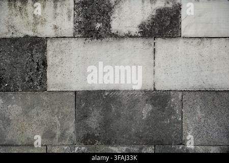 A textured background featuring a weathered wall made of mixed light and dark grey concrete blocks. Shows signs of aging, grunge, and rough. Stock Photo