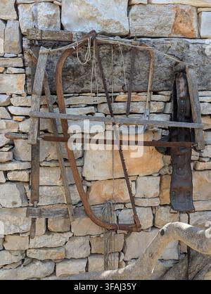 A collection of aged antique woodworking tools and hand saws on a traditional rustic stone wall with a coastal village background in Croatia Stock Photo