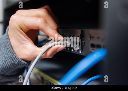 Close-up of a technician's hands organizing and plugging blue and grey ethernet network cables into a network switch. Stock Photo