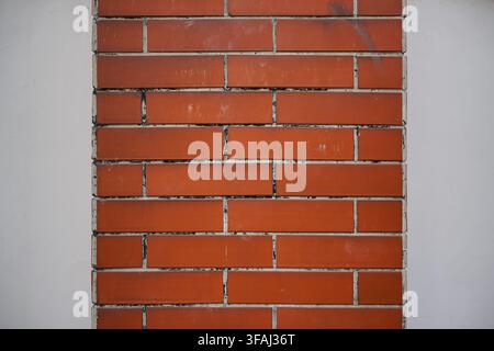 Close up of a red brick pillar section surrounded by smooth white concrete walls. Architectural texture background showing contrast between rough. Stock Photo