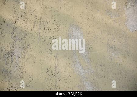 Close up of a weathered pale yellow painted concrete wall showing peeling, chipped paint, dark mold spots, and rough grunge texture. Ideal for vintage Stock Photo