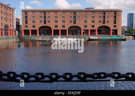 A scenic view across the water at Royal Albert Dock in Liverpool, UK, featuring historic brick warehouses with red columns and moored boats Stock Photo