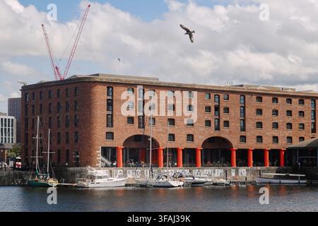 A scenic view across the water at Royal Albert Dock in Liverpool, UK, featuring historic brick warehouses with red columns and moored boats Stock Photo