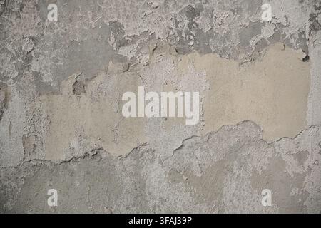 Close up of an old grey concrete wall with layers of fading beige paint peeling off. Detailed grunge texture showing natural decay. Stock Photo