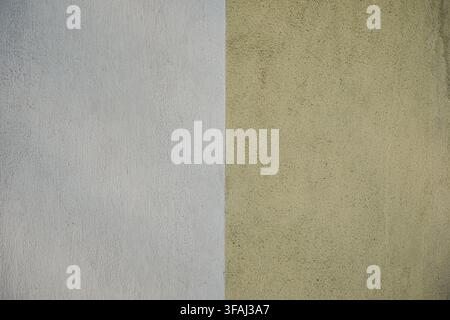 Close up view of a textured wall painted in two contrasting colors, featuring a vertical split between bright white and pale yellow. Stock Photo
