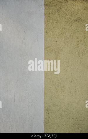 Vertical divide on a textured exterior wall featuring pale yellow and bright white paint. Abstract dual color background showing rough stucco. Stock Photo