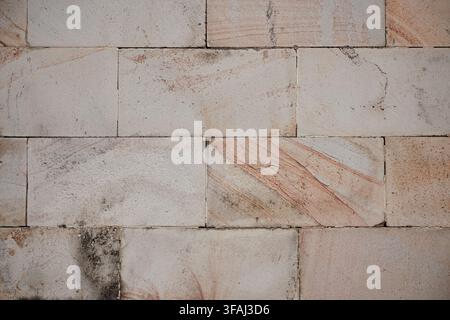 Close up view of a masonry wall made of rectangular stone blocks featuring natural red and pink veining. Weathered architectural surface. Stock Photo